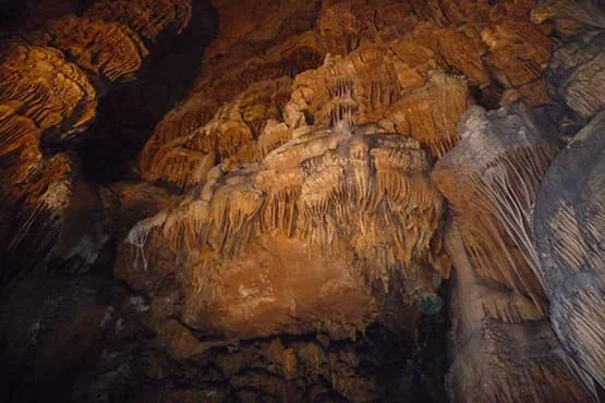 Concrétions calcaires dans une grotte éclairée de tons orangés.